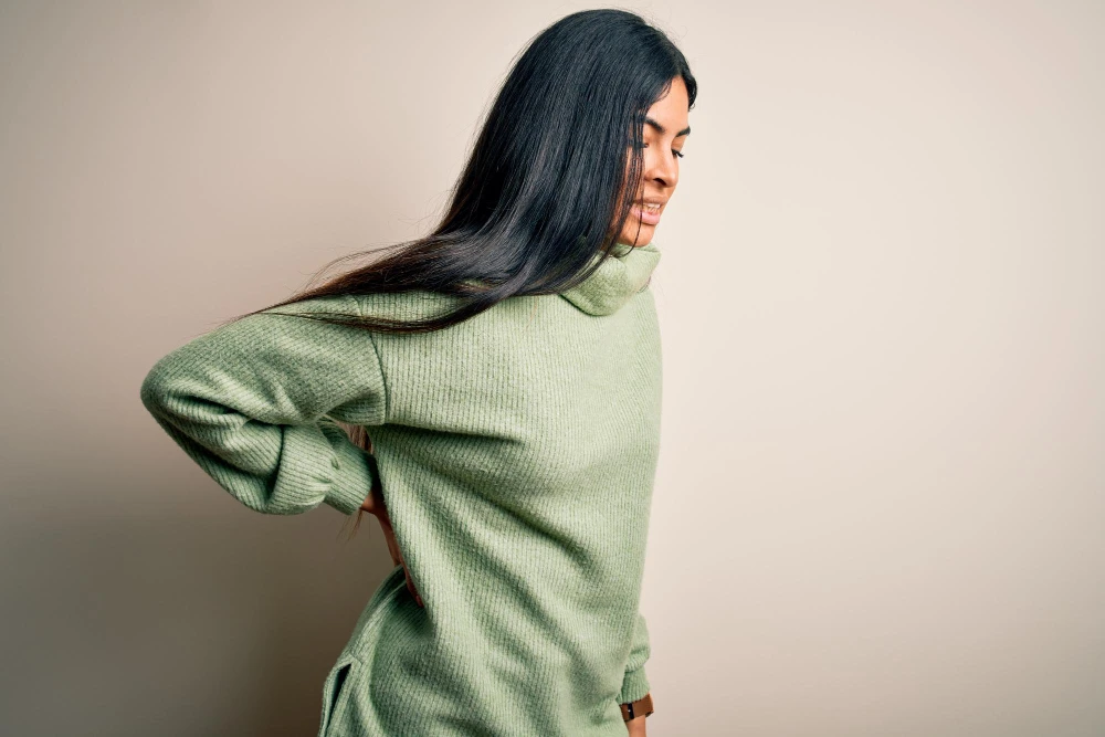 cosa-fare-mal-di-schiena-Donna con maglione verde che si tocca la parte bassa della schiena con espressione lievemente dolorante